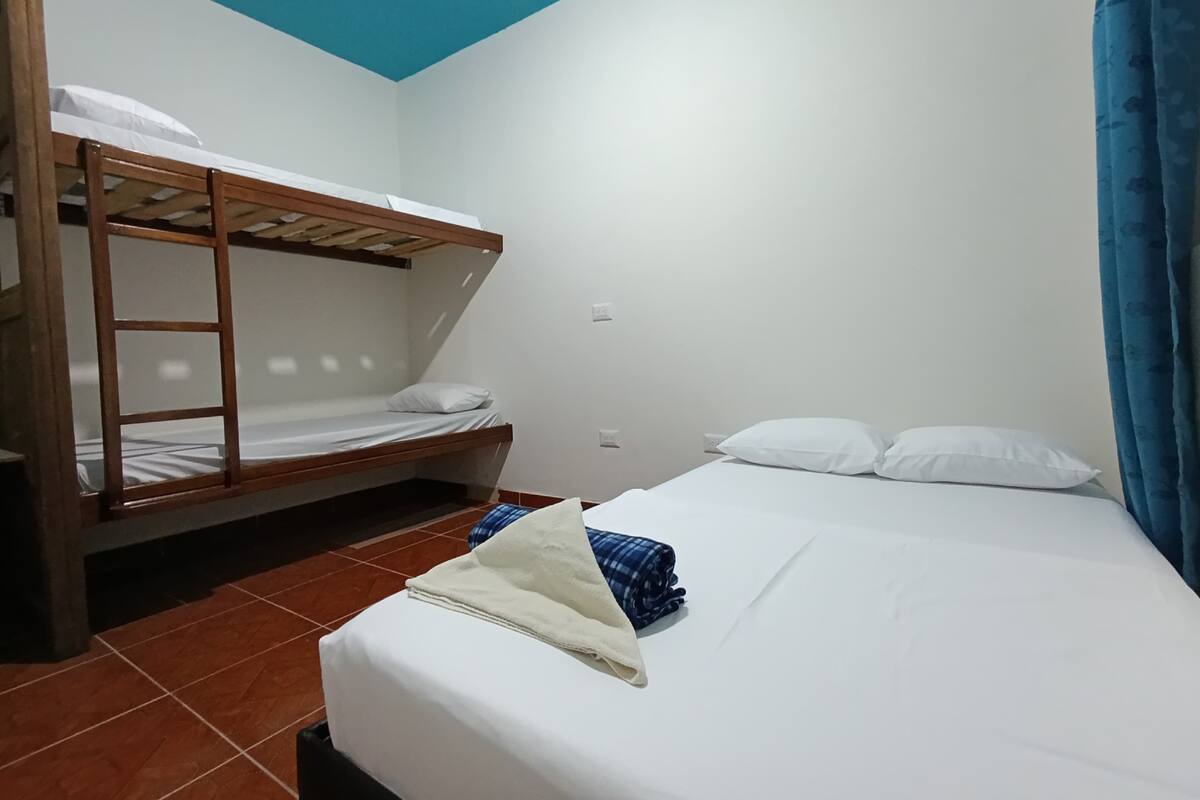 Une chambre avec un lit superposé, un lit simple et un rideau bleu.