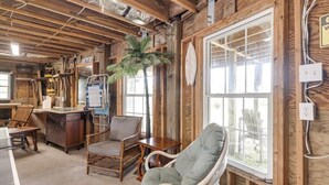Un interior rústico con vigas de madera, un ventanal grande, muebles de mimbre y una pequeña mesa.