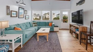 Una sala de estar con techo de madera, un sofá color turquesa, una mesa de centro, un televisor y una estantería.