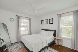 A bedroom with a bed, a ceiling fan, a window with curtains, a wall clock, and three framed pictures.