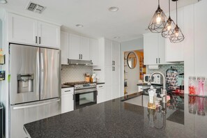 A modern kitchen with stainless steel appliances, white cabinetry, and a granite countertop. - ATX Retreat • N. Central • Pool Spa Grill Sundeck Golf Pad• 15 min to Downtown (Austin)