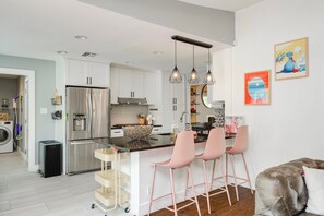 Una cocina moderna con electrodomésticos de acero inoxidable, una isla central con taburetes de bar y un comedor con sofá y mesa de centro.