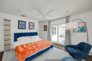 A bedroom with a bed, a blue chair, a ceiling fan, and artwork on the walls.