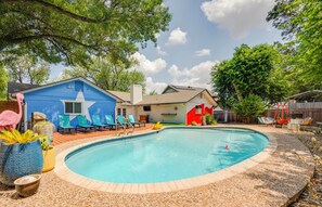 A backyard with a swimming pool, lounge chairs, and a blue building with a star mural.