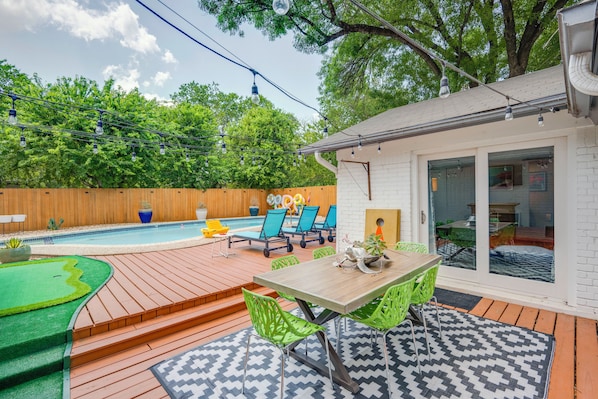 A backyard with a wooden deck, a pool, and a patio area with a table and chairs.