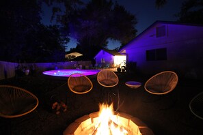 A backyard with a fire pit, lounge chairs, and a swimming pool.