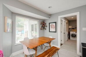 A dining area with a wooden table and chairs, a window with blinds, and a framed picture on the wall.