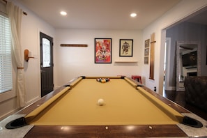 A pool table with a white cue ball, surrounded by a wooden frame, in a room with white walls and a door with a window.