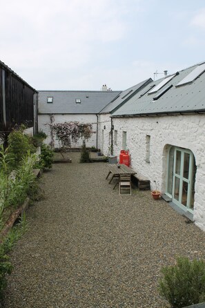 Relax in a serene courtyard surrounded by lush greenery and a charming stone building.