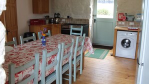 Una cocina compacta con armarios de madera, una mesa de comedor con sillas, una lavadora y un ventanal pequeño.
