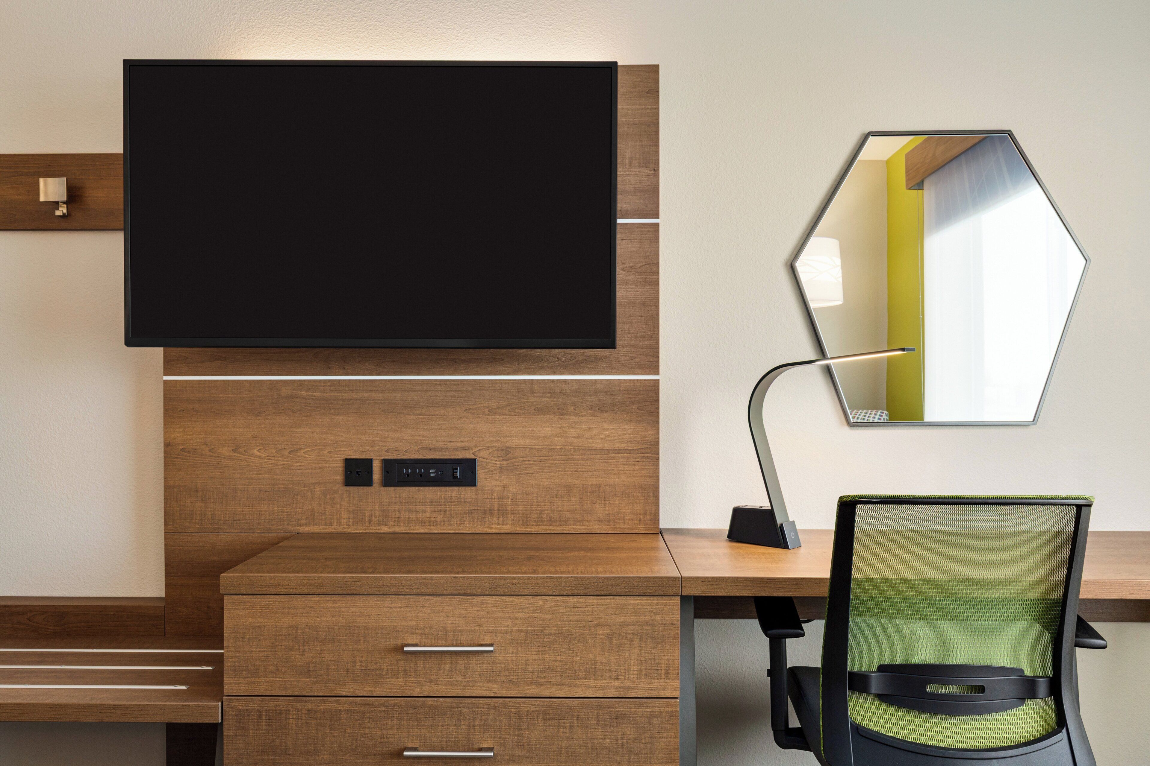 Un espacio de oficina moderno con una televisión de pantalla grande montada en una pared de madera, un escritorio con una silla y un espejo que refleja parte de la habitación.