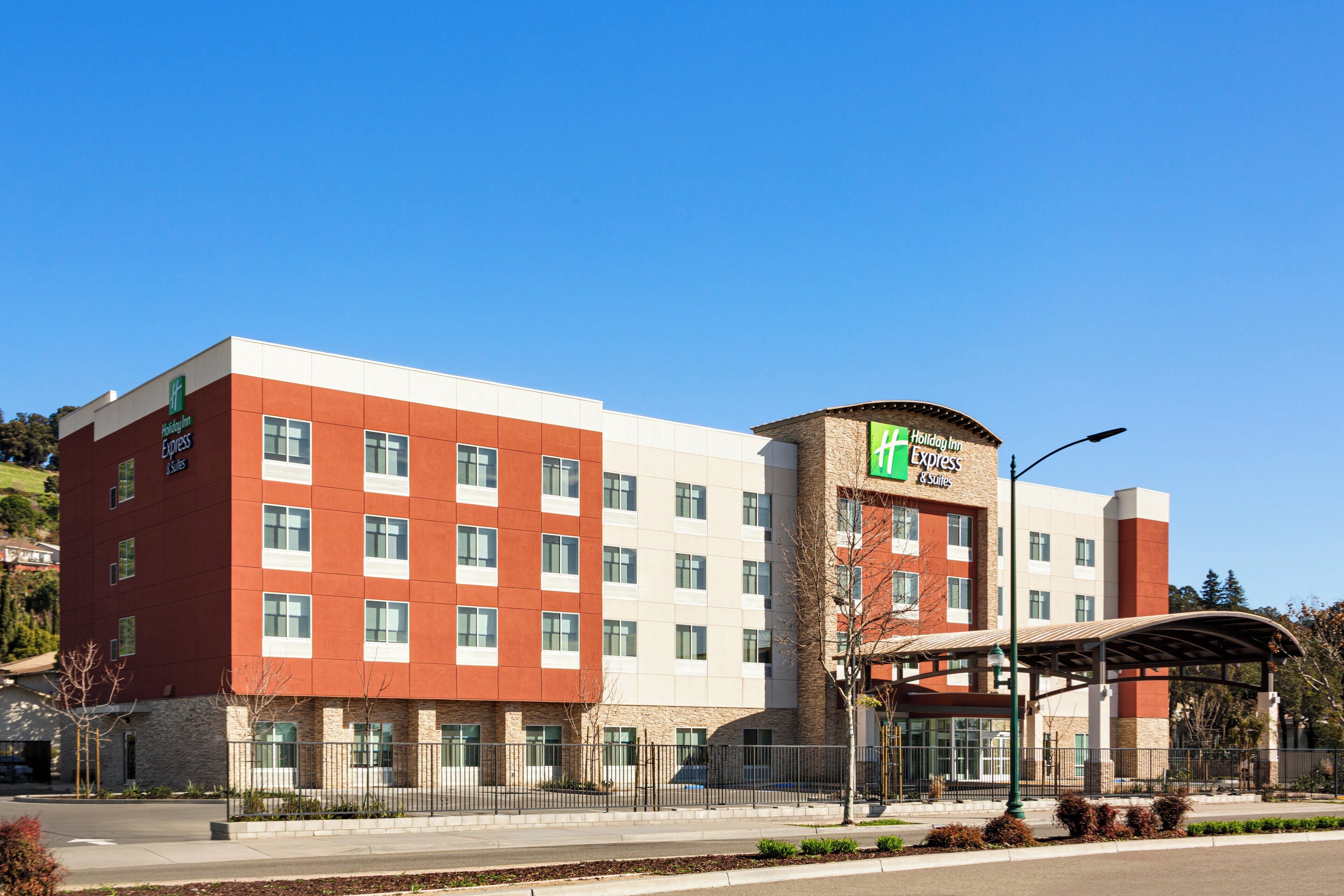 Un hotel Holiday Inn Express con un diseño moderno, que presenta una combinación de colores rojo y blanco en su fachada, varios pisos y una zona de entrada cubierta.