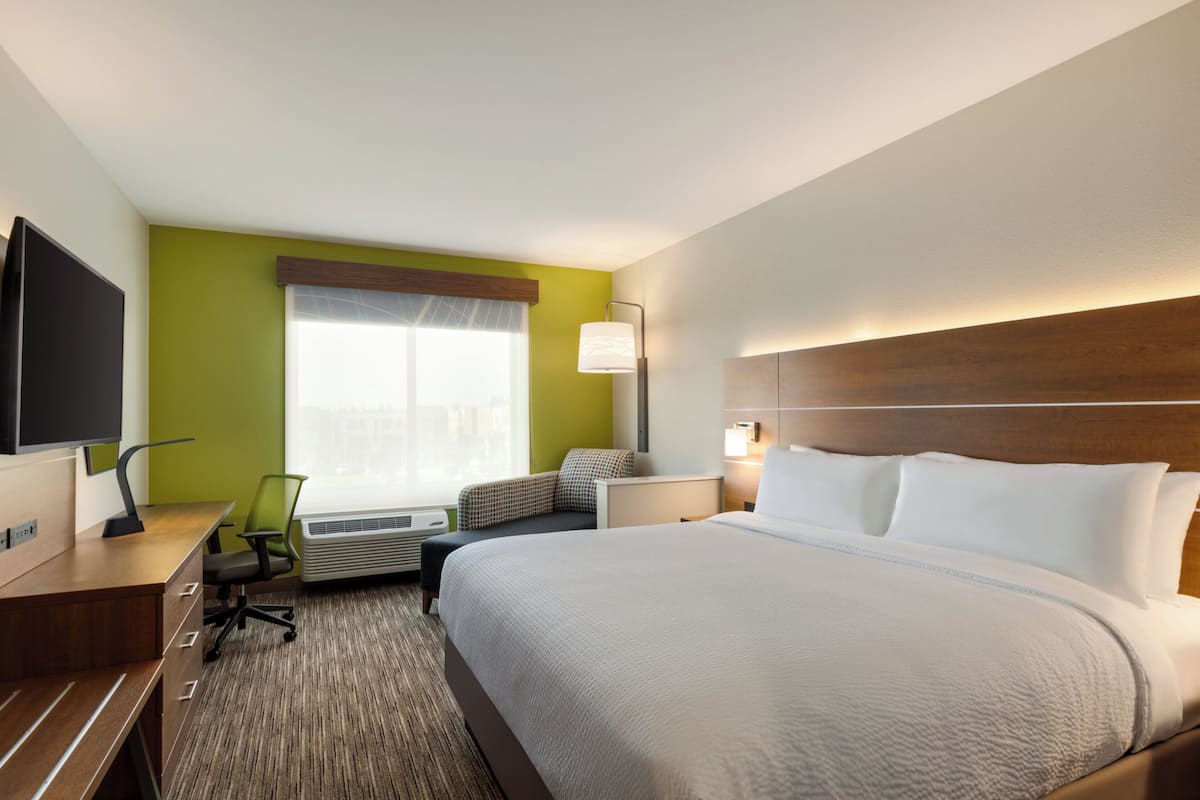 A hotel room with a large bed, a desk with a flat-screen TV, a chair, and a window with curtains.