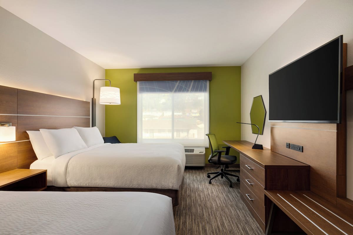 A hotel room with two beds, a desk with a chair, a flat-screen TV, and a window with a view of the outside.