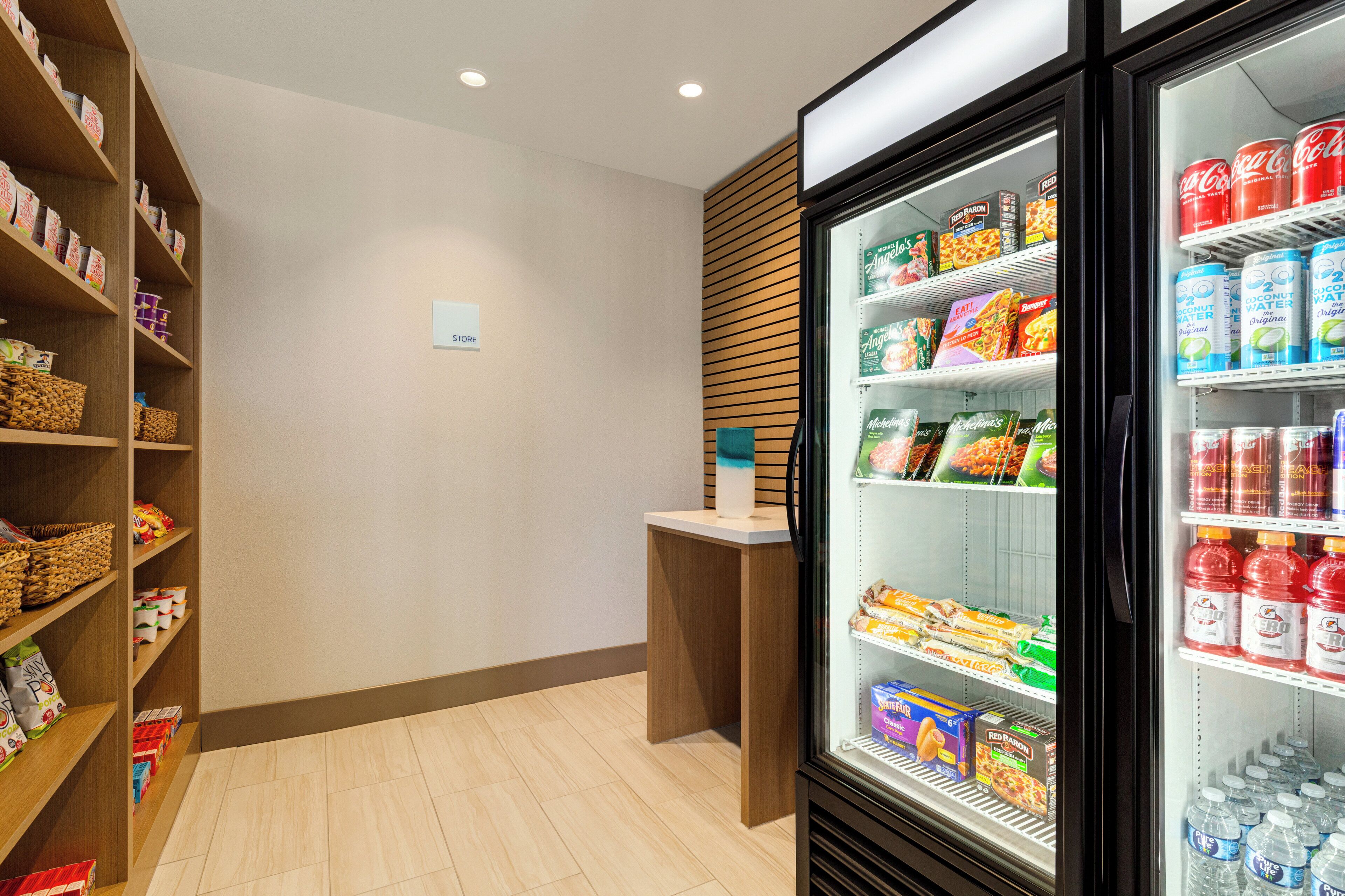 A clean, well-organized snack and beverage area with shelves stocked with snacks, boxed goods, and bottled drinks.