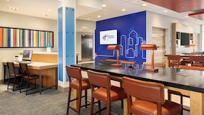 A modern hotel lobby with a reception desk, seating area, and a blue wall with a cityscape design. - Holiday Inn Express & Suites Hayward - Castro Valley by IHG (Hayward)