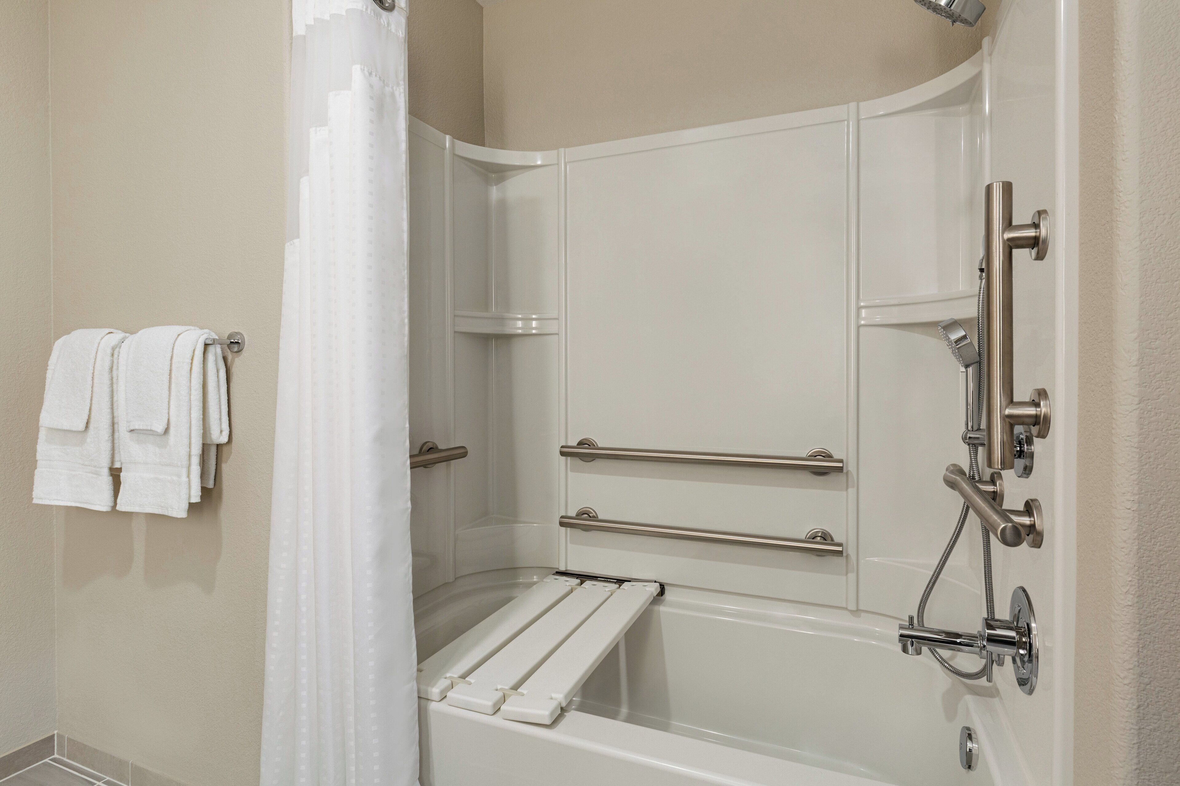 A corner shower with a white bathtub, grab bars, and a showerhead.