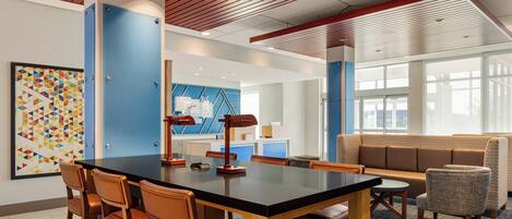 Um saguão de hotel moderno com uma grande mesa de conferências, assentos confortáveis e uma obra de arte geométrica colorida na parede.