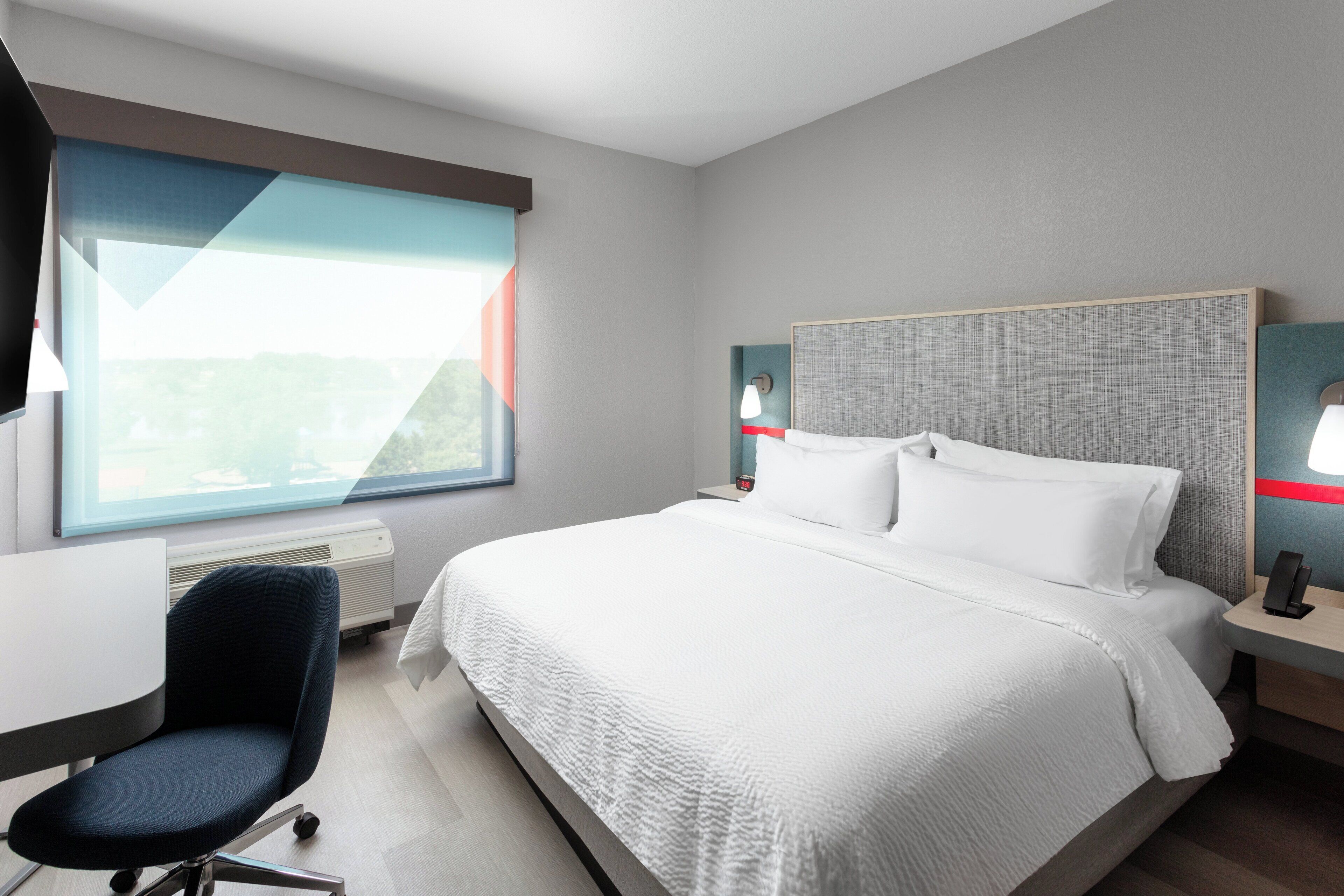 A modern hotel room with a large bed, a desk, and a chair.