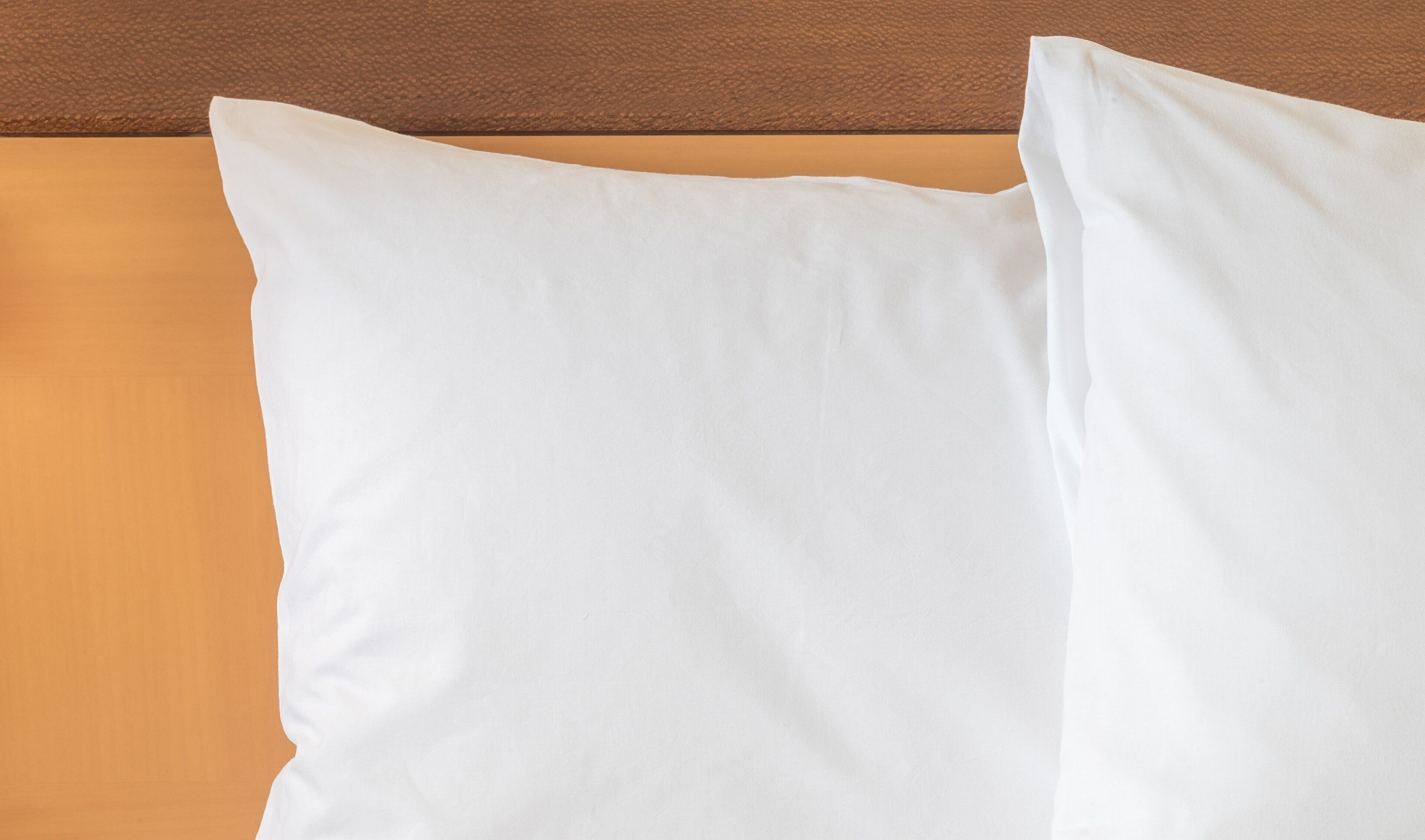 A white pillow against a textured brown headboard.