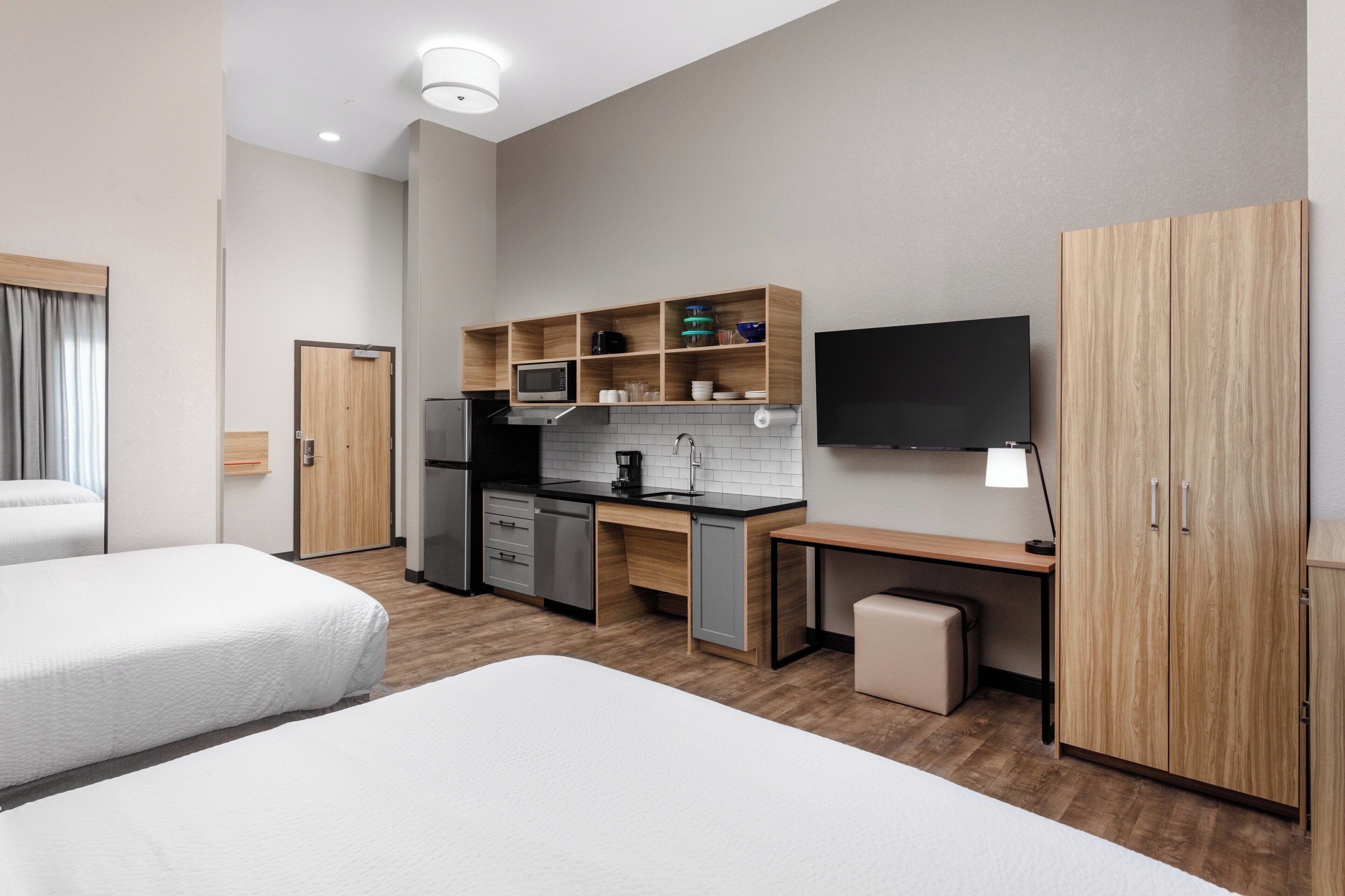 Ein Hotelzimmer mit zwei Betten, einer Küchenzeile, einem Fernseher und einem Kleiderschrank.