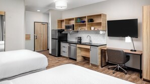 Una habitación de hotel moderna con kitchenette, televisión de pantalla plana, escritorio y dos camas.
