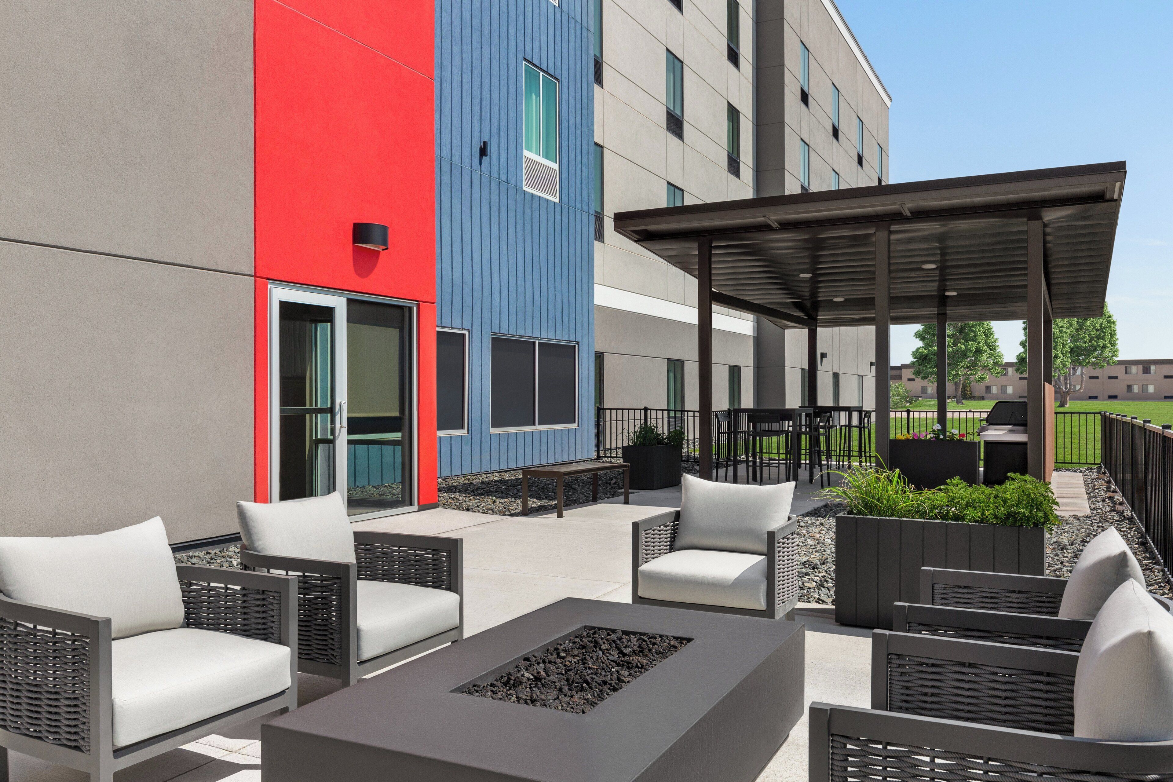 An outdoor seating area with wicker chairs and a fire pit, adjacent to a building with a red and blue facade.