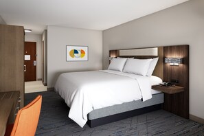 A modern hotel room with a large bed, a wooden nightstand, a desk, and a chair.