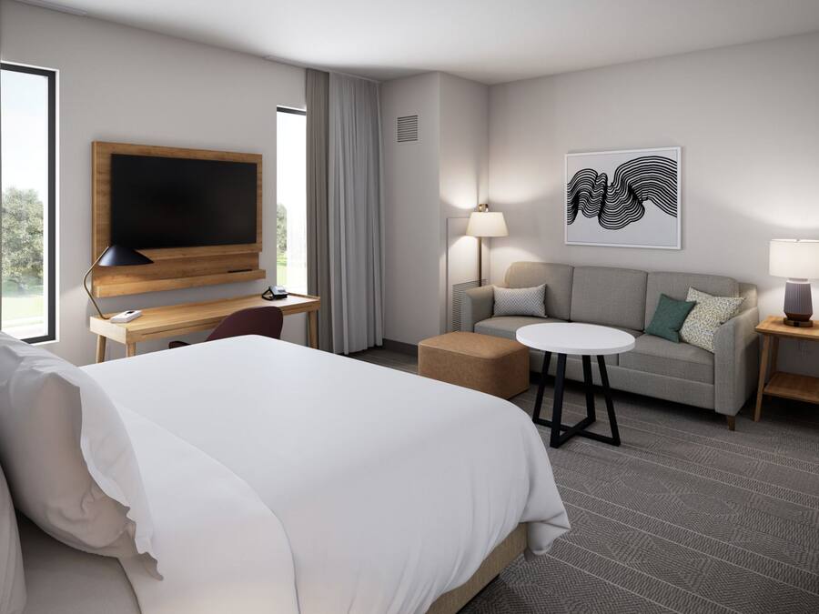 Ein Hotelzimmer mit einem Bett, einem Schreibtisch mit Flachbildfernseher, einer Couch, einem runden Tisch und zwei Lampen.