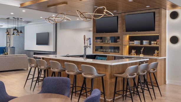 A modern kitchen with a central island, bar stools, and a large flat-screen TV mounted on the wall. - Staybridge Suites Port Elgin by IHG (Saugeen Shores)