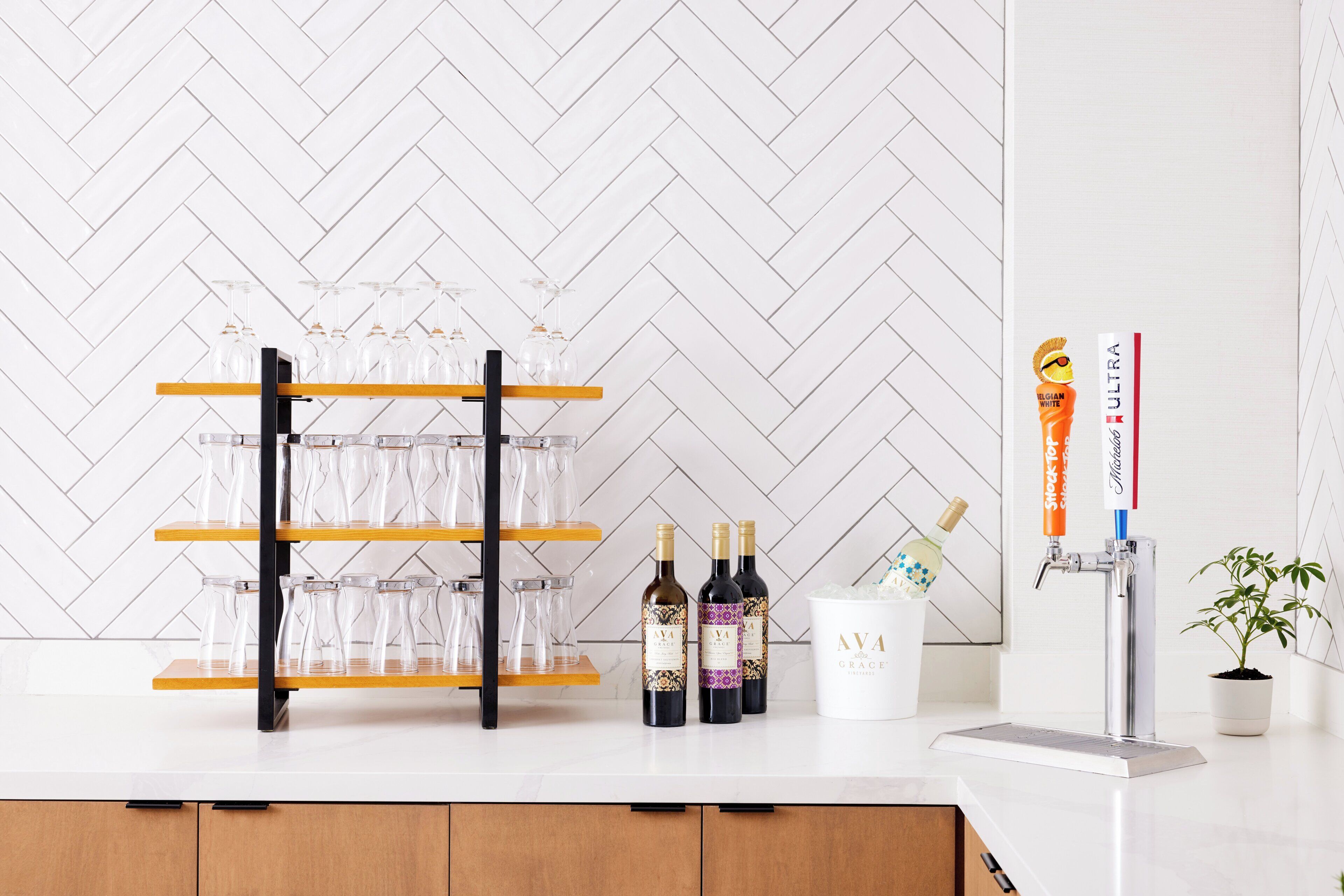 Zona de bar con una estantería para vinos, botellas, copas y un grifo identificado como 'AVA GRACE'.