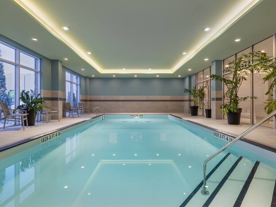 Una piscina interior con agua cristalina, rodeada de sillones de descanso y plantas en macetas.