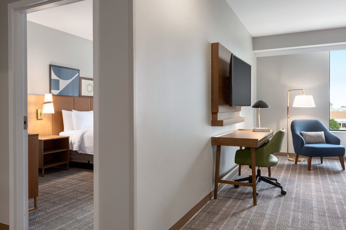 A hotel room with a bed, desk, chair, TV, and a view of the outdoors.