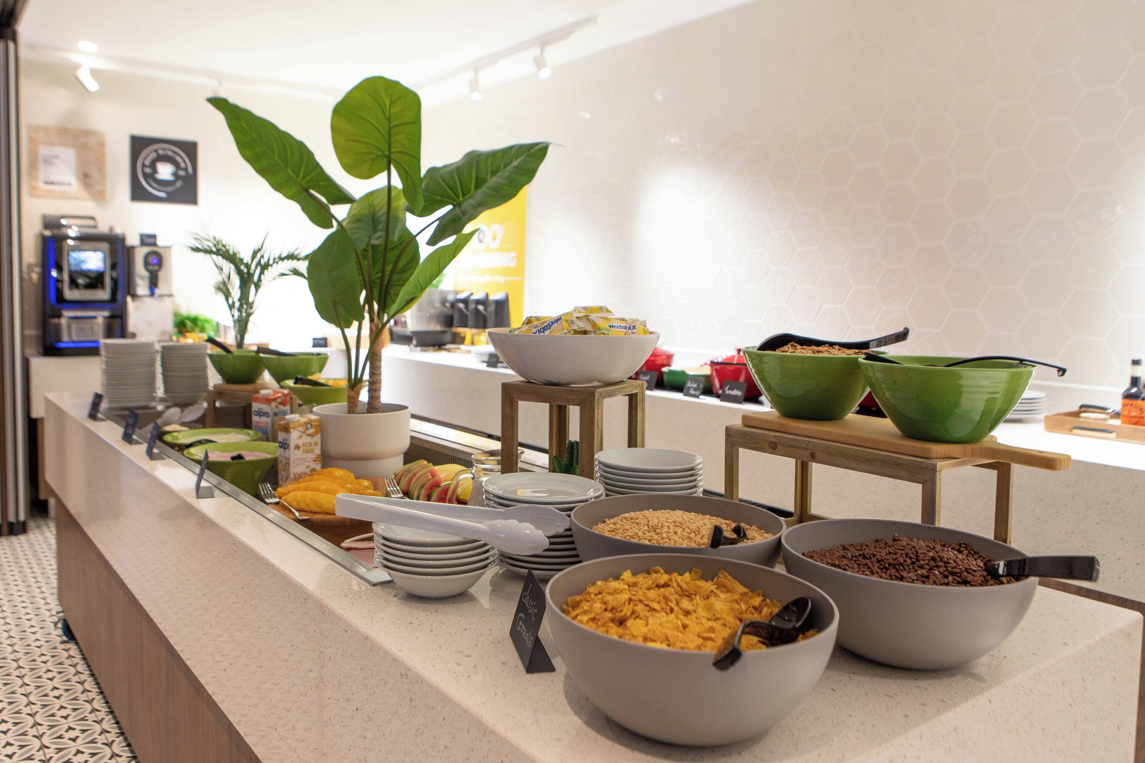 A buffet with various food items and bowls, a coffee machine, and a potted plant in a hotel setting.