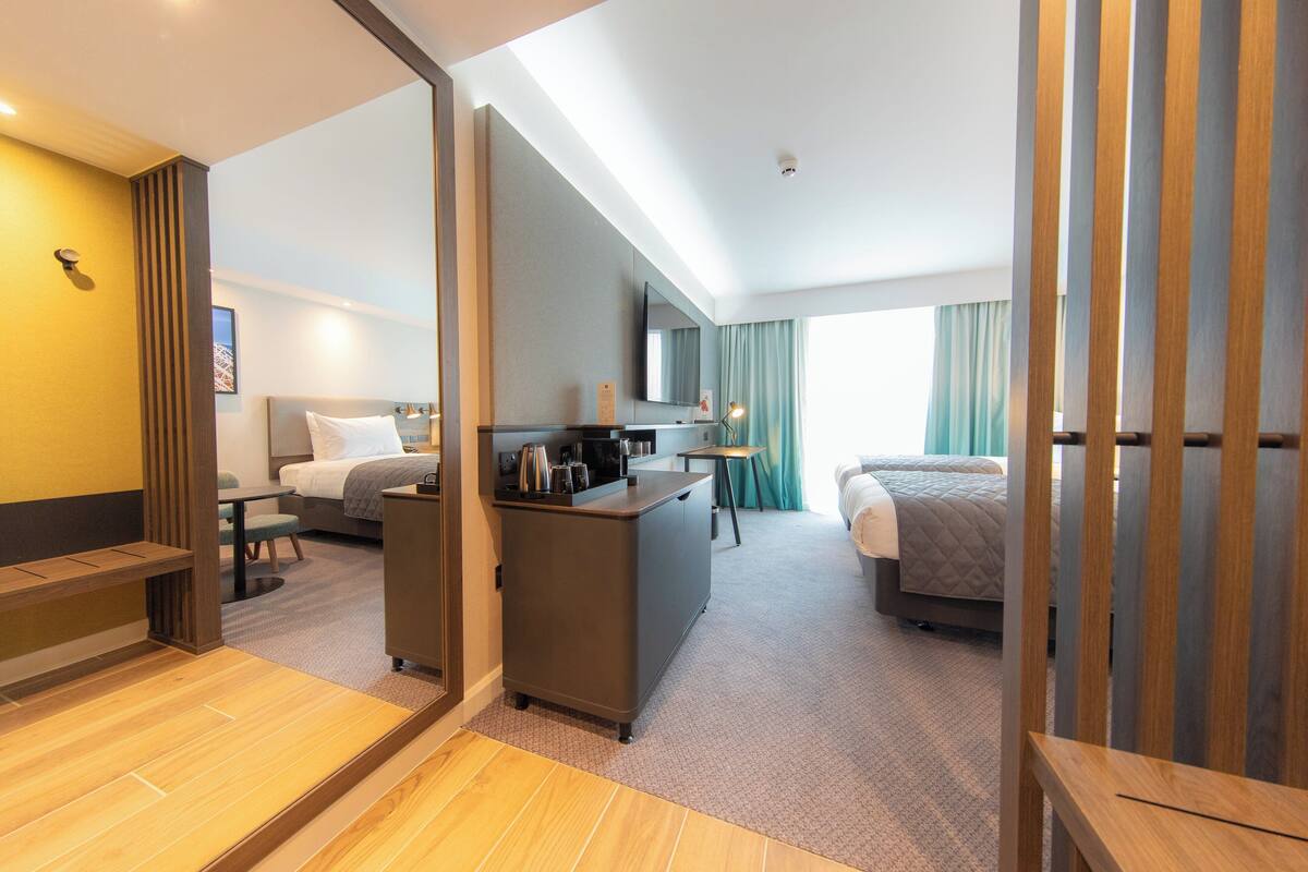 Ett hotellrum med en säng, ett skrivbord, en stol, en tv och ett fönster med gardiner.