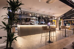 A modern bar area with a herringbone wood floor, bar stools, and a variety of bottles and glasses on shelves. - Holiday Inn Blackpool by IHG (Blackpool)