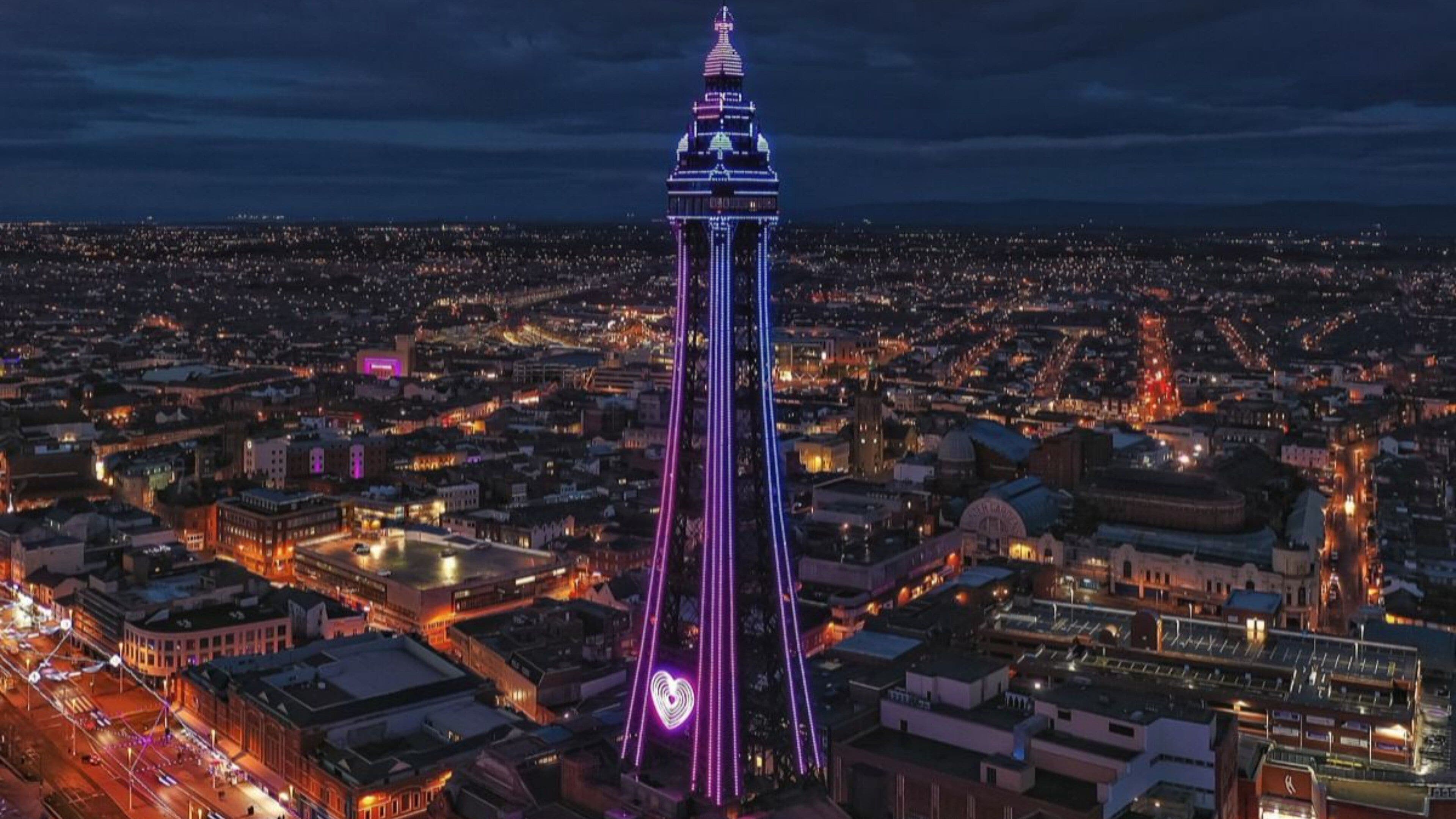 Une haute tour, ornée de bandes lumineuses verticales, se dressant au milieu d’un paysage urbain nocturne.