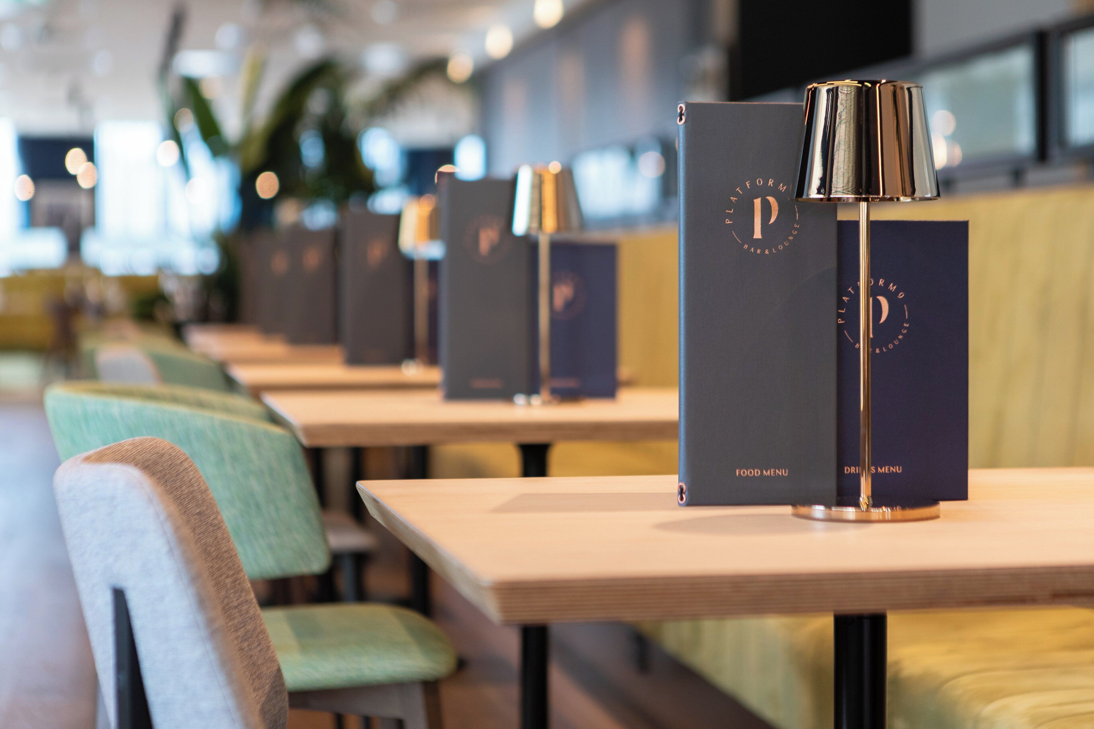 Een rij tafels met donkerblauwe menukaarten en een goudkleurige lamp op elk.