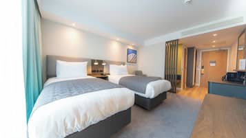 A hotel room with two beds, a desk, and a kitchenette.