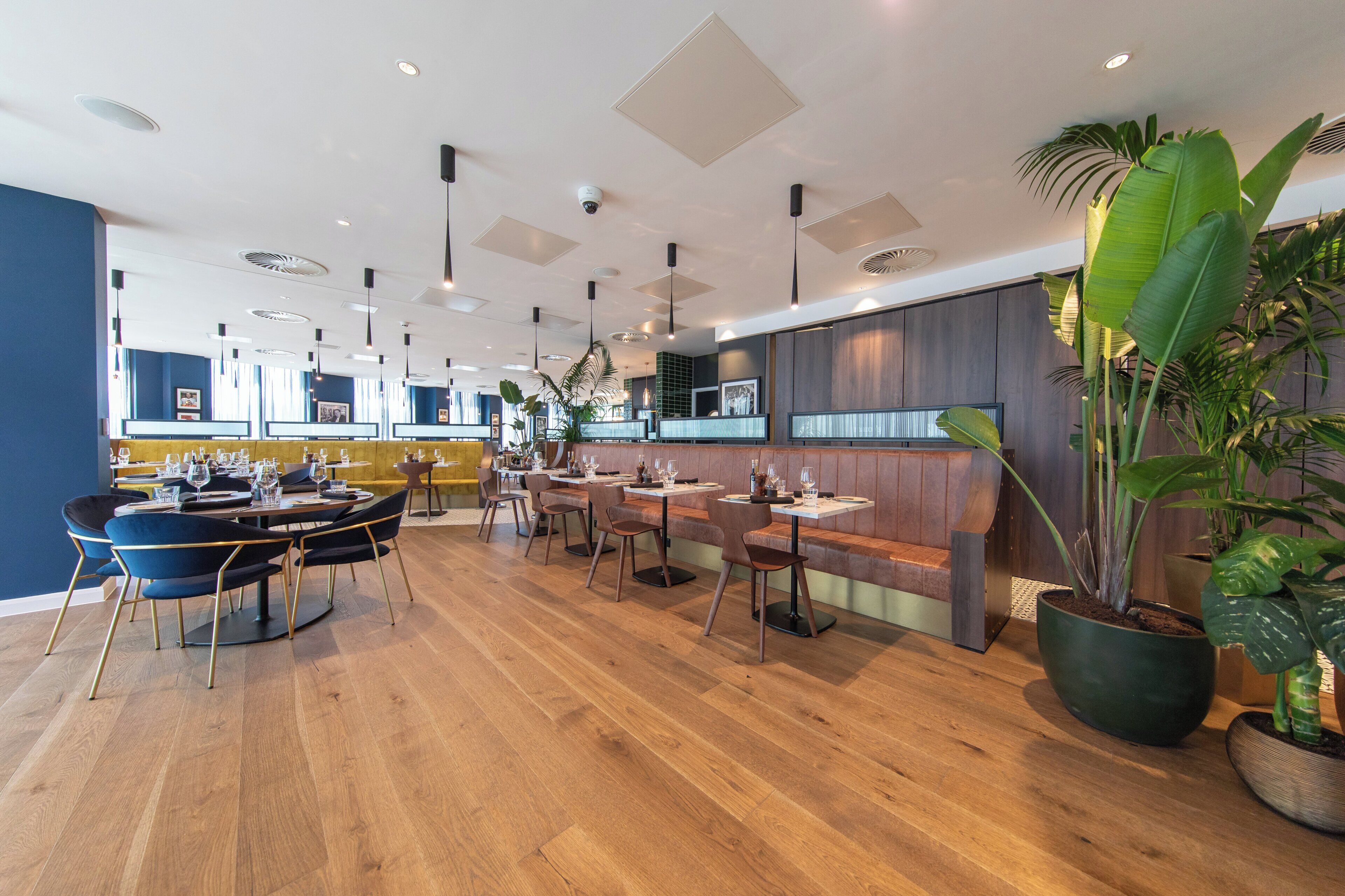 A modern restaurant interior with wooden flooring, multiple dining tables, and booths.