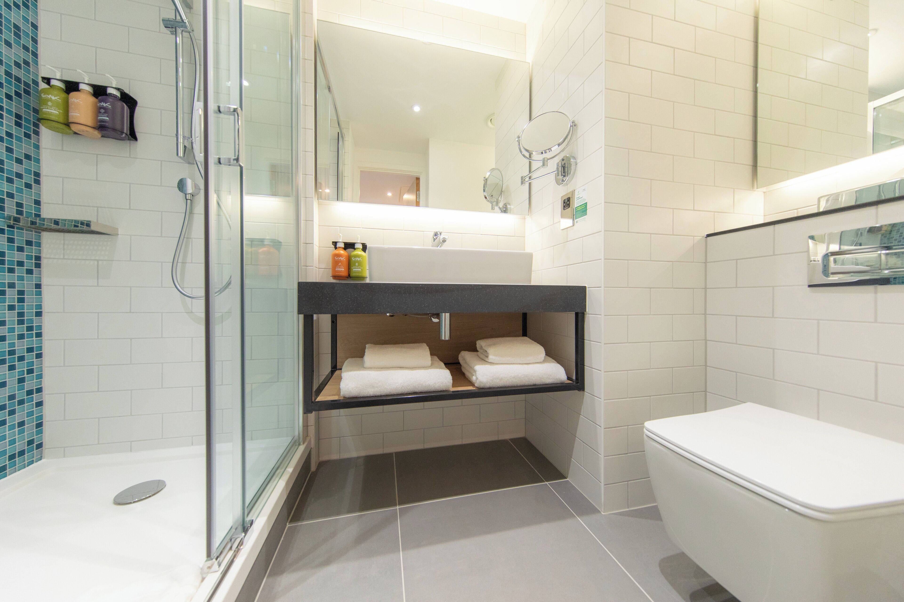 Un baño moderno con ducha envuelta en vidrio, inodoro blanco y tocador con espejo.