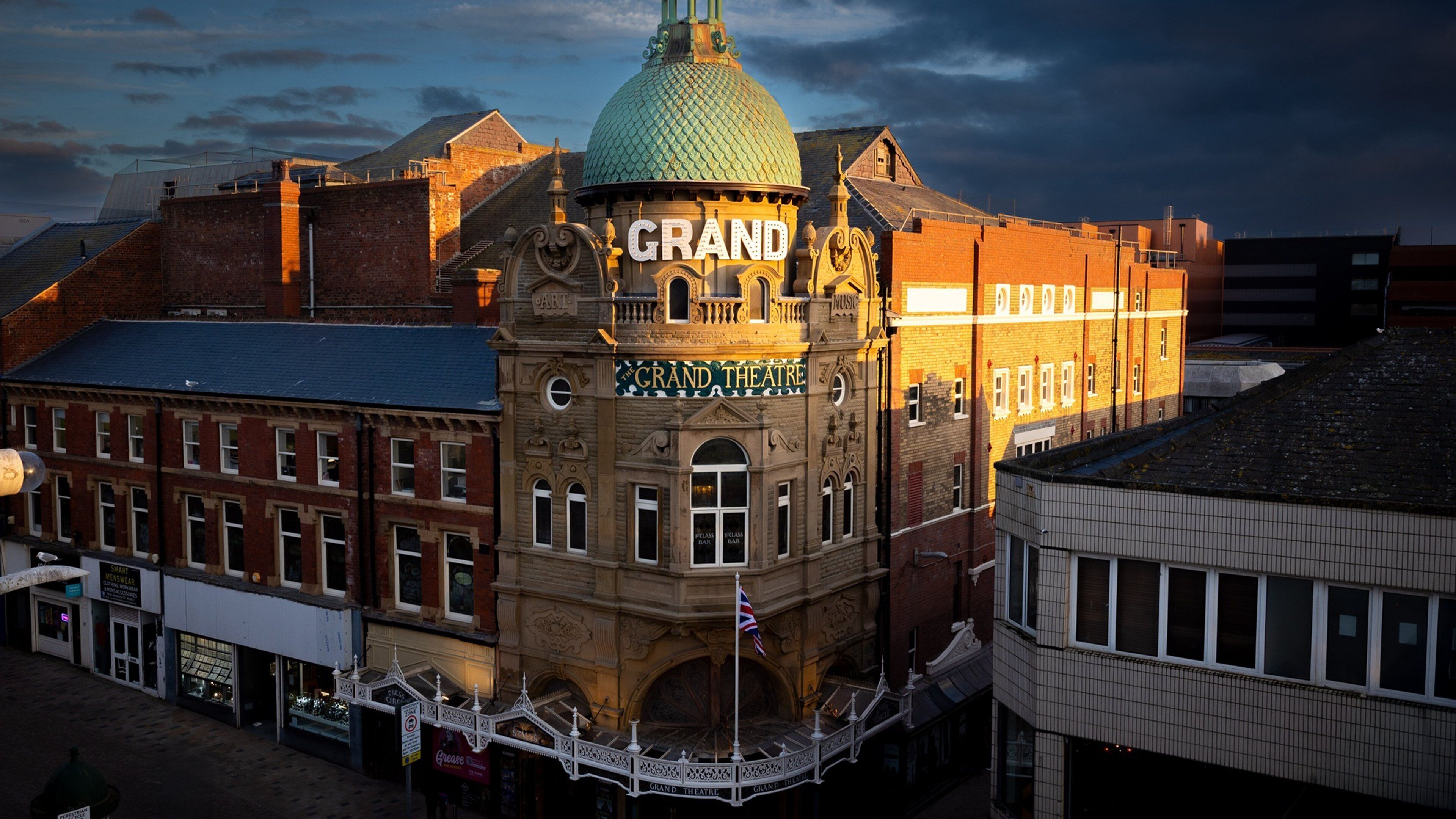 A historic building with a prominent clock tower, a dome, and a sign reading 'Grand Theatre.'
