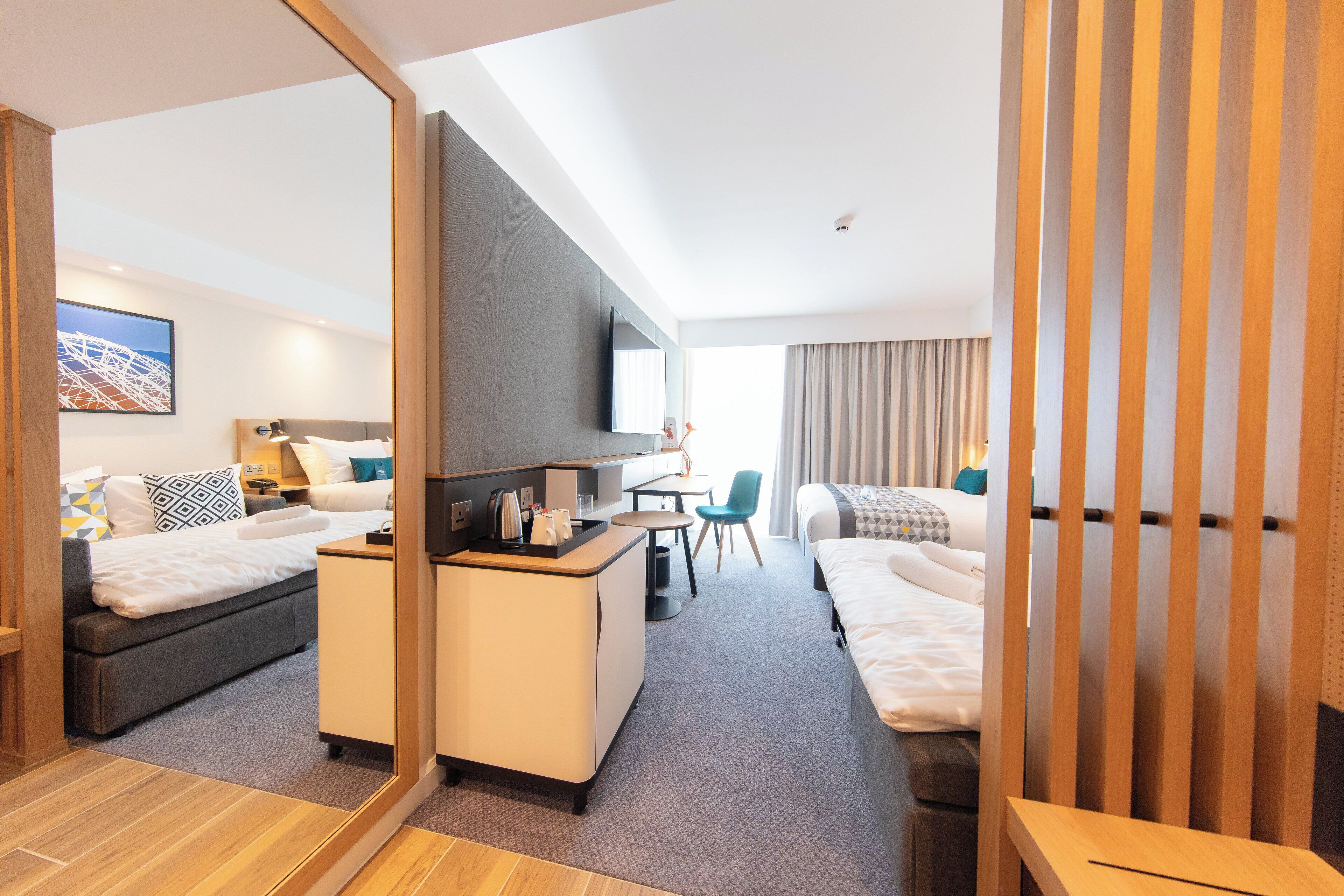 A modern hotel room with a bed, a desk, a chair, and a TV.