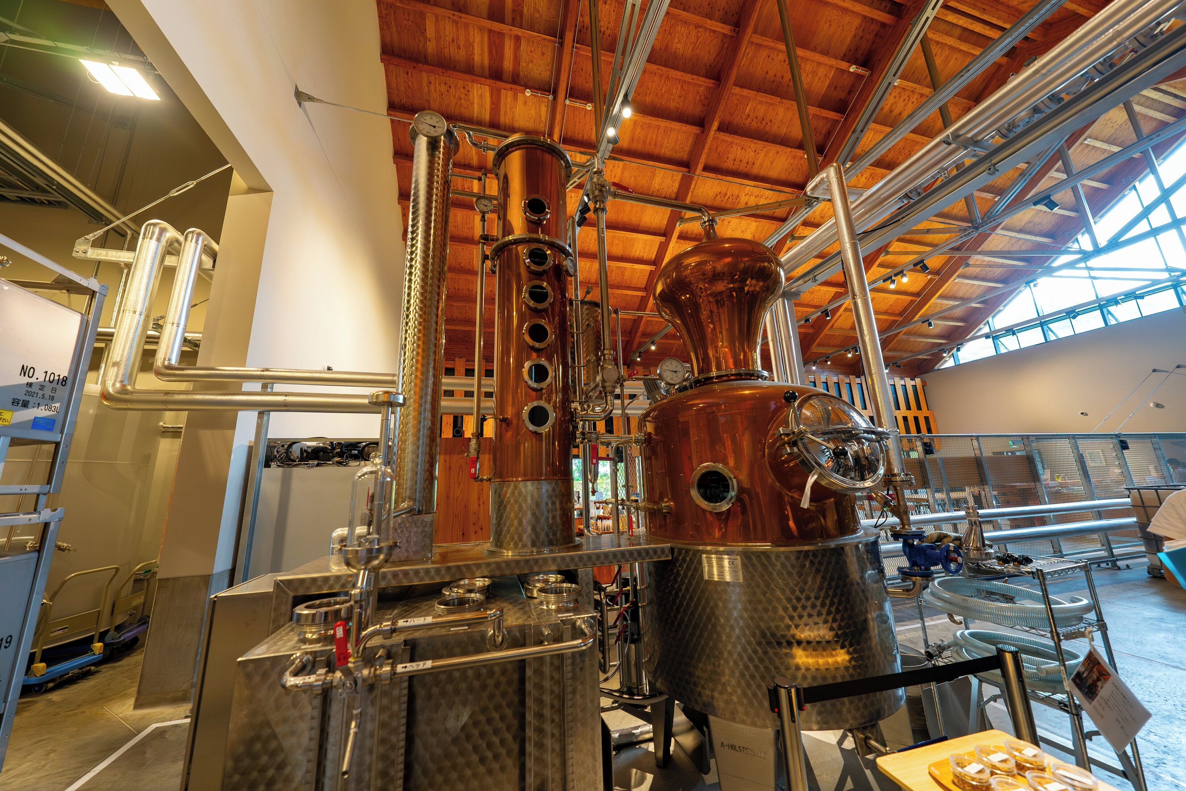 A distillery interior with large copper stills, wooden beams, and a high ceiling.