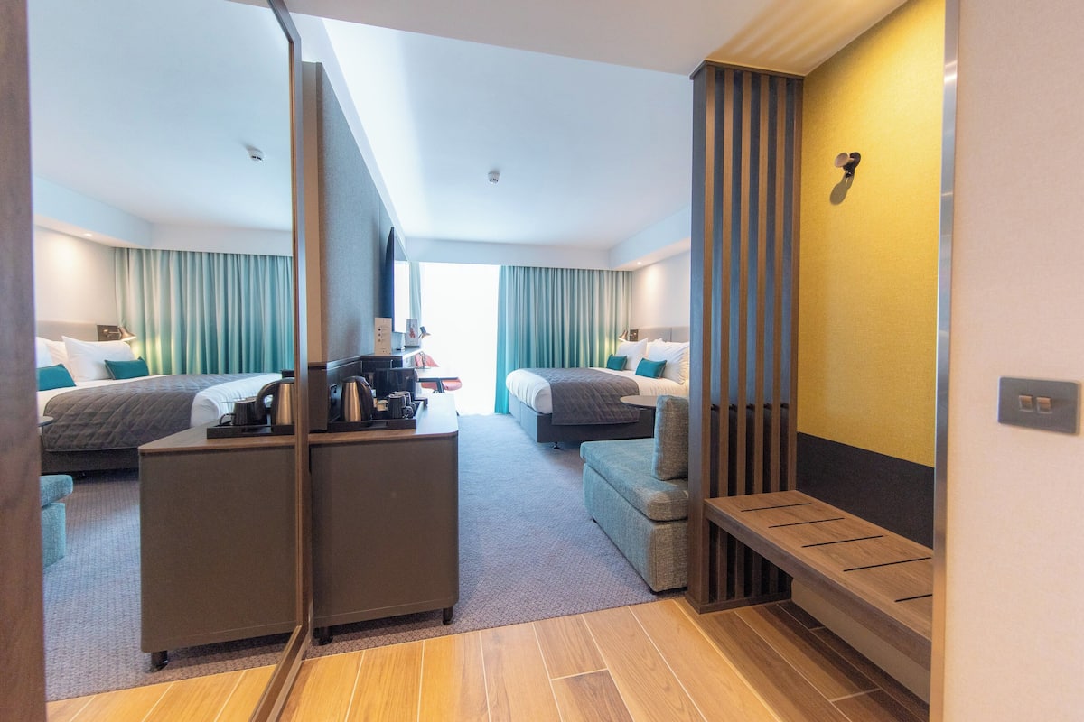 Ett modernt hotellrum med två sängar, ett skrivbord, en bänk och utsikt över staden.