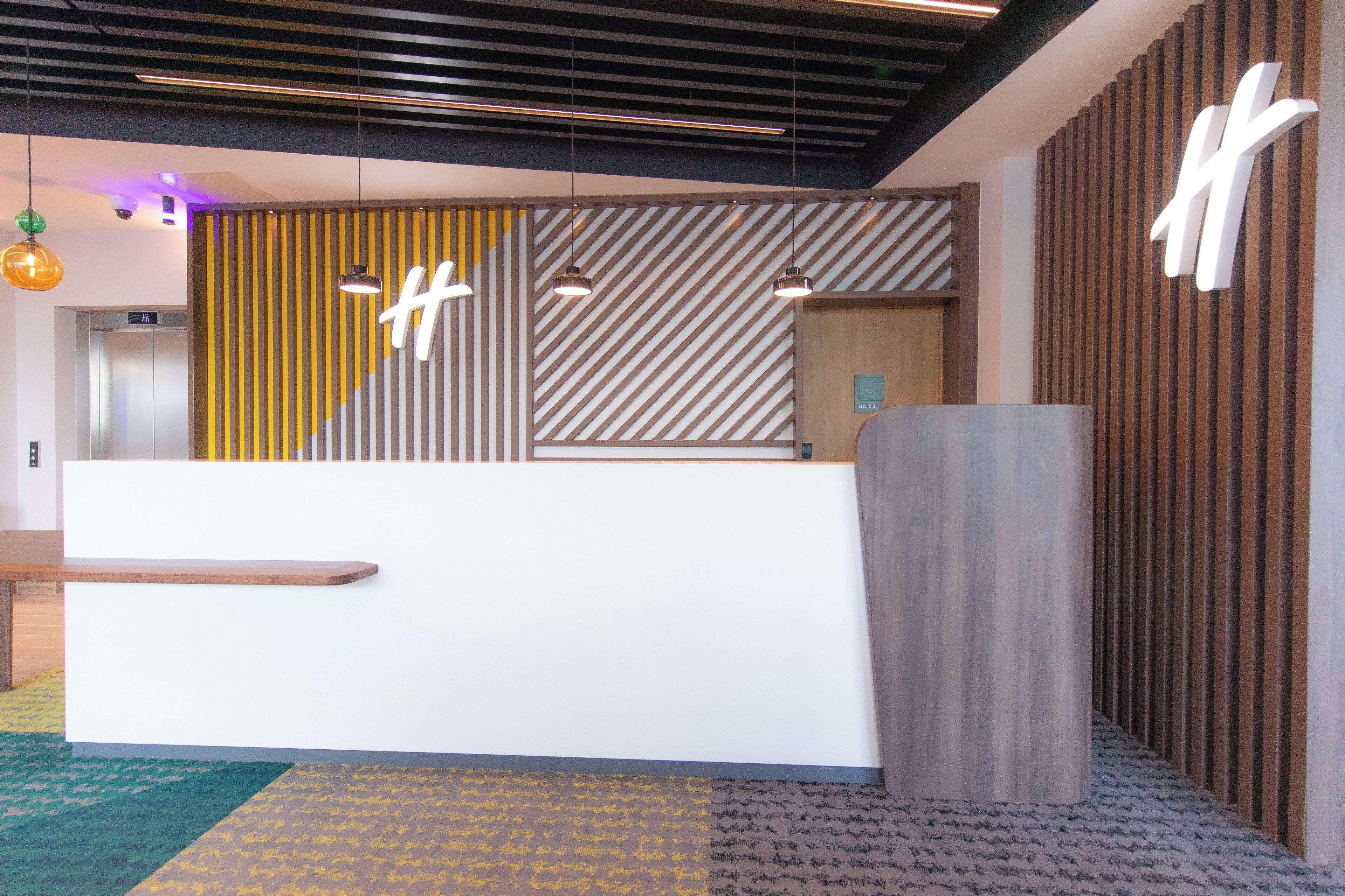 Een receptiegedeelte met een modern design, met een receptiebalie, een wand van houtpanelen en een groot 'H'-logo.