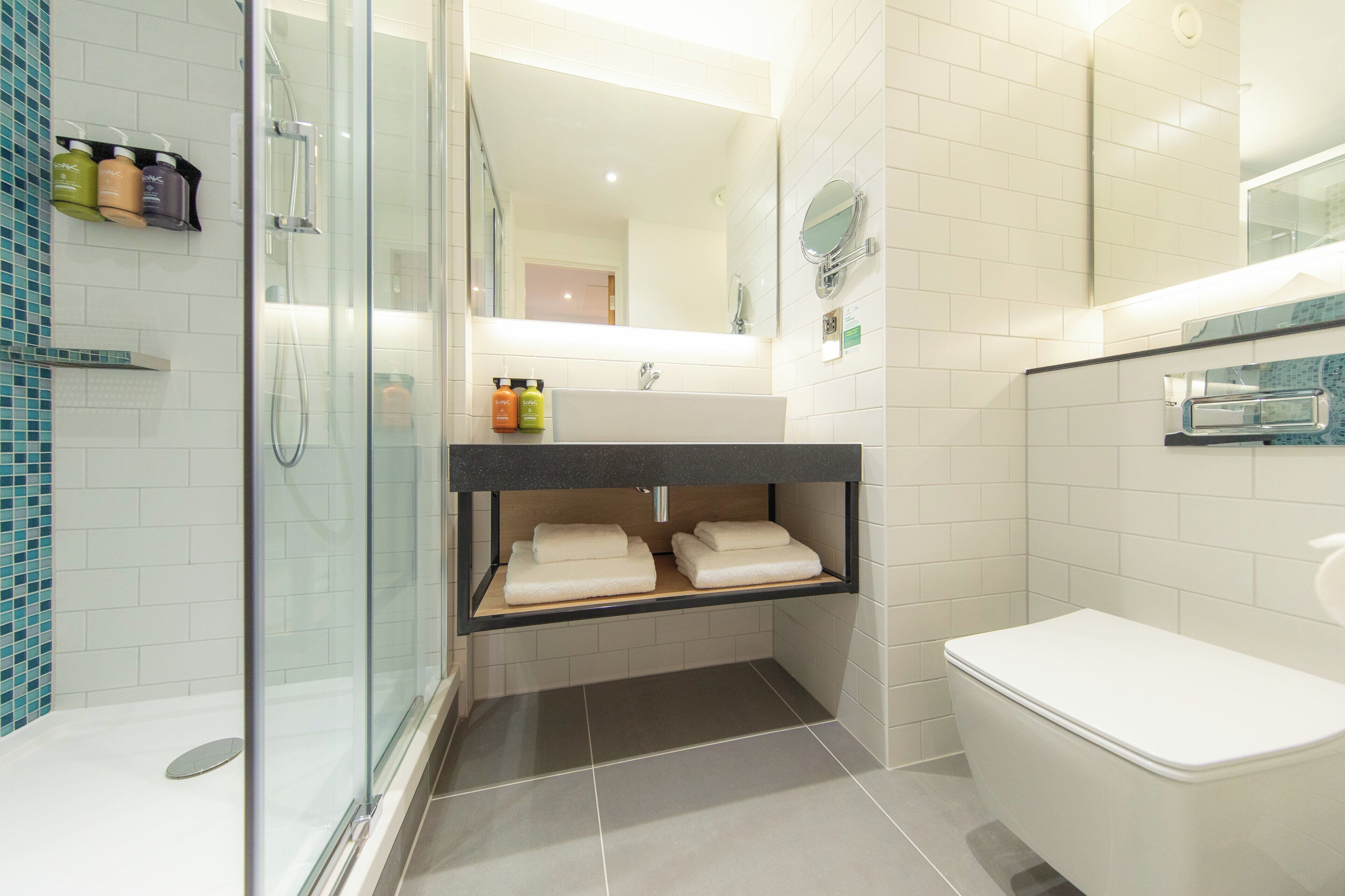 Een moderne badkamer met een douchecabine van glas, een wit toilet en een wastafel met spiegel.