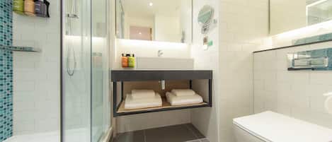 Un baño moderno con cabina de ducha de vidrio, inodoro blanco y tocador con espejo.