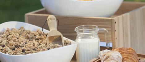 Dos tazones blancos con granola y cereal, una jarra de leche y un cruasán sobre una bandeja de madera.