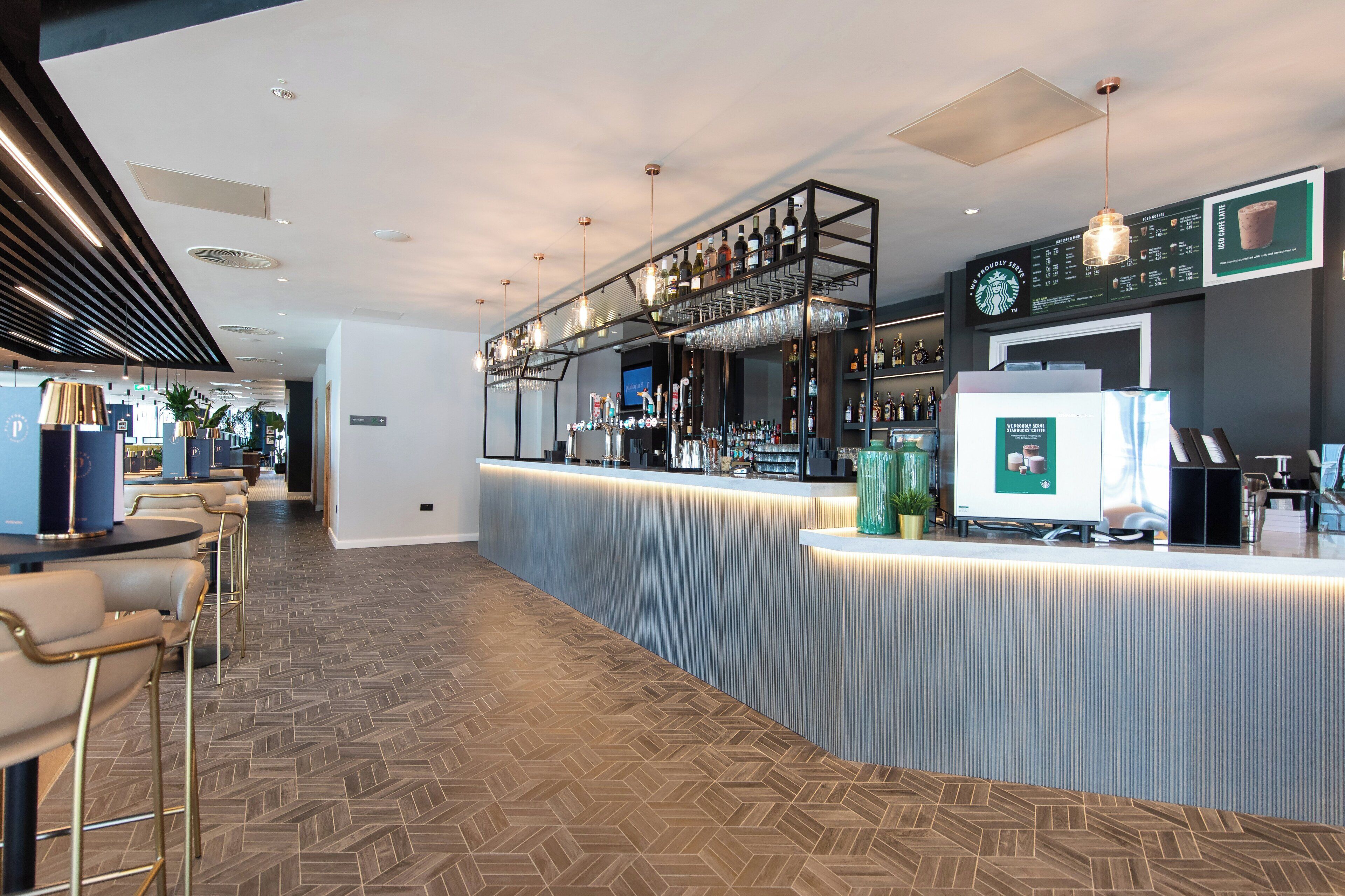 A modern bar area with a long counter, bar stools, and a variety of bottles and glasses.